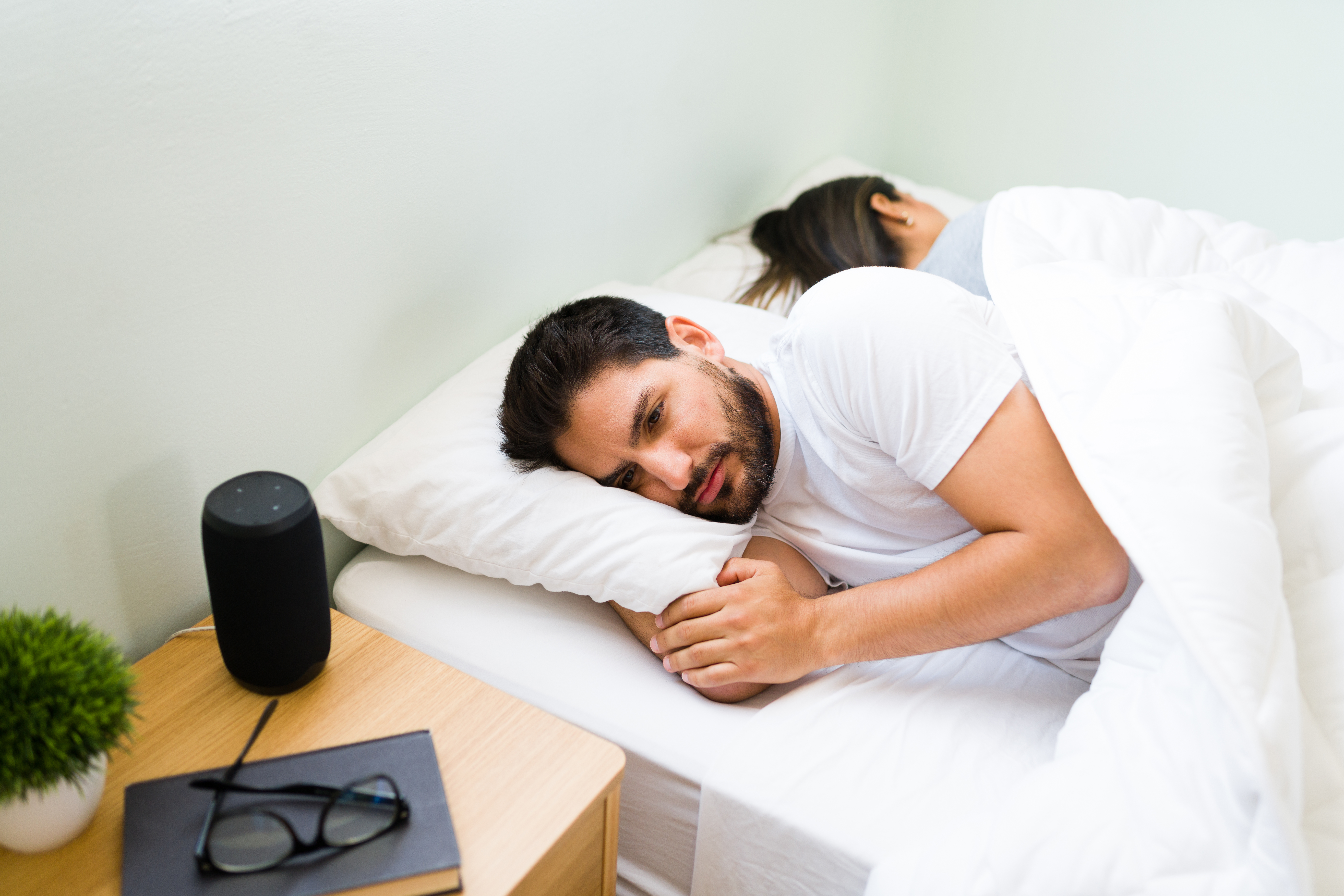 Man lying awake in bed next to his partner, showing signs of poor sleep or insomnia